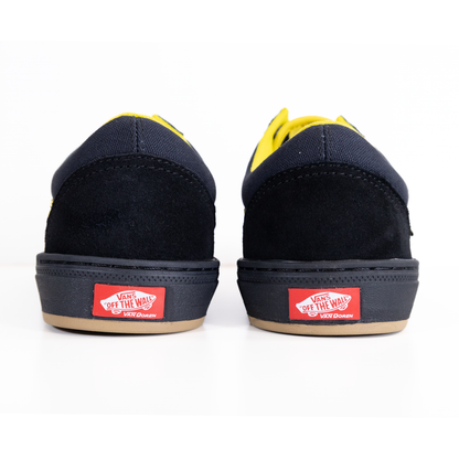 Black sneakers with yellow accents and red Vans labels on a white background
